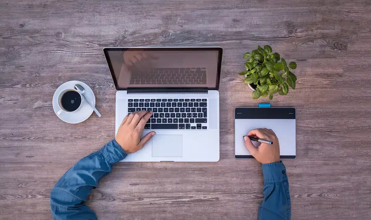 Étudiant·e à une table de travail avec ordinateur portable et carnet, jour lumineux